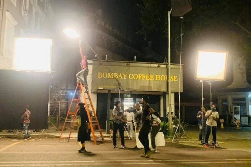 A group of people working on a streetlight near a building labeled 'Bombay Coffee House.' 2