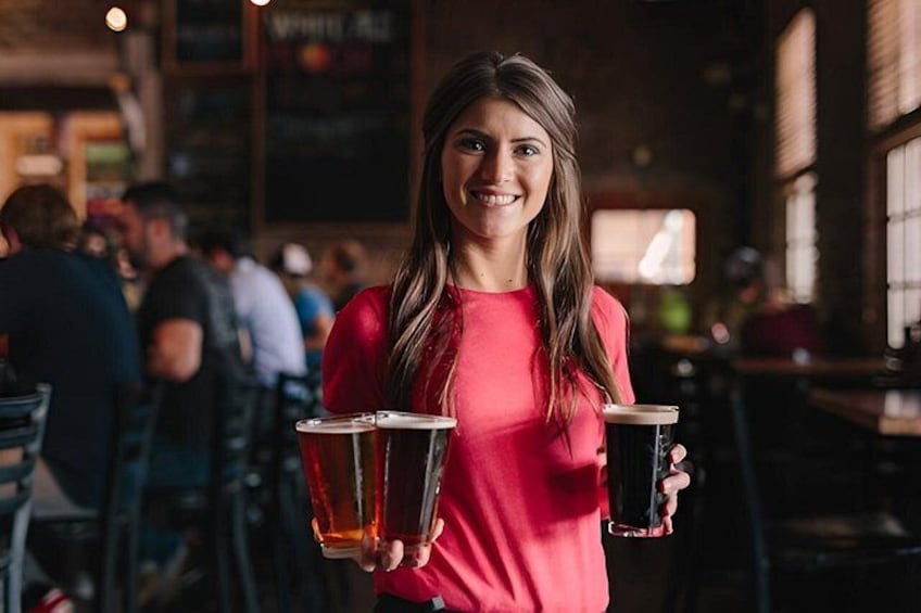 Une personne tenant deux verres de bière dans un bar, avec d’autres clients en arrière-plan. 1