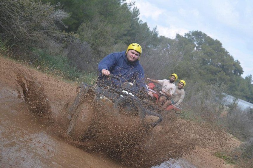 A person riding a quad bike through a muddy area with splashes of water. 3