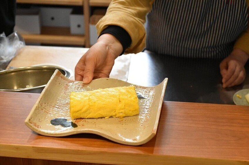A person holding a rolled omelette on a ceramic plate. 5