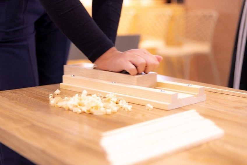 A person using a woodworking tool on a wooden surface with wood shavings scattered around. 3