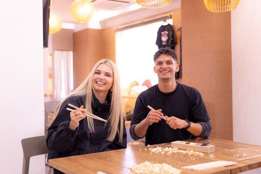Two people sitting at a table with chopsticks and a wooden block, possibly engaged in a cooking or food preparation activity. 5