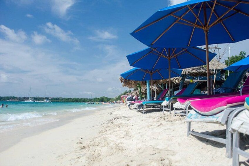 Una playa con arena blanca, sombrillas azules y sillones de playa coloridos. 4
