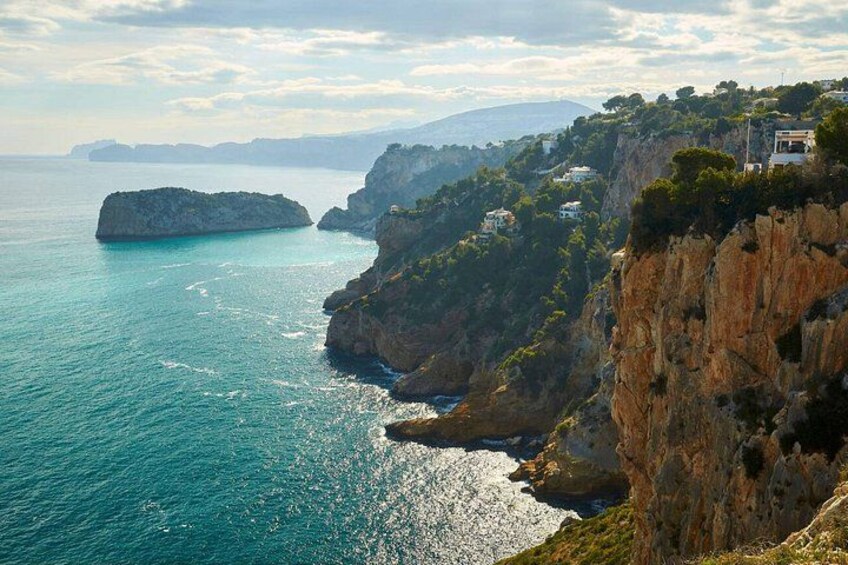 Un paisaje costero con acantilados, una pequeña isla y edificios a lo largo del risco. 1
