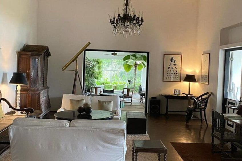 Una sala de estar con un sofá blanco, un armario de madera, una mesa con lámpara y un ventanal con vistas a la vegetación. 3