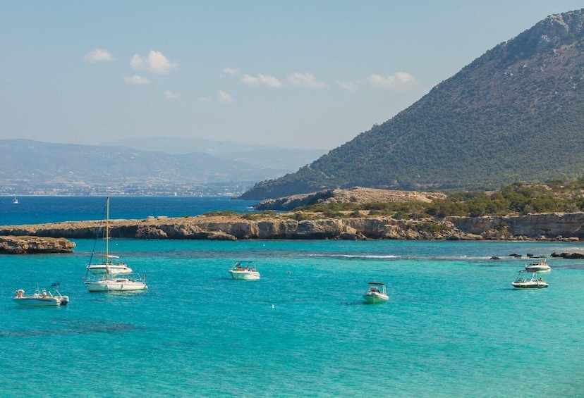 A coastal scene with boats on turquoise water, rocky cliffs, and a distant cityscape. 3