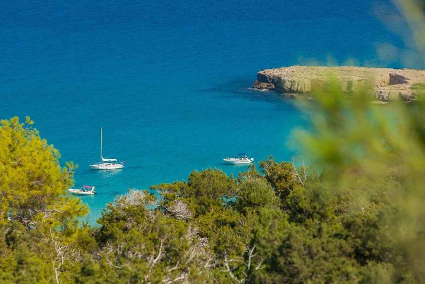 A coastal landscape with clear turquoise waters, a rocky outcrop, and several boats anchored near the shore. 1