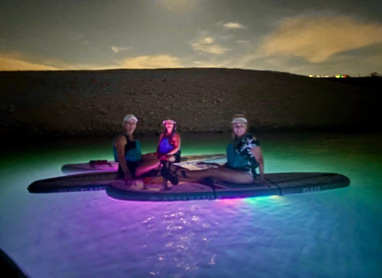 Three people on a paddleboard in a body of water at night. 2
