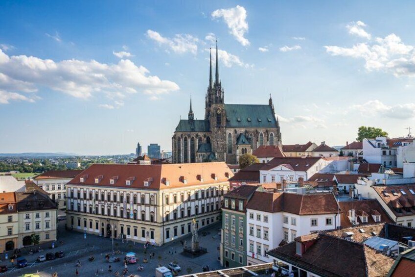 A cathedral with a tall spire, a square with buildings, and a clear sky. 1