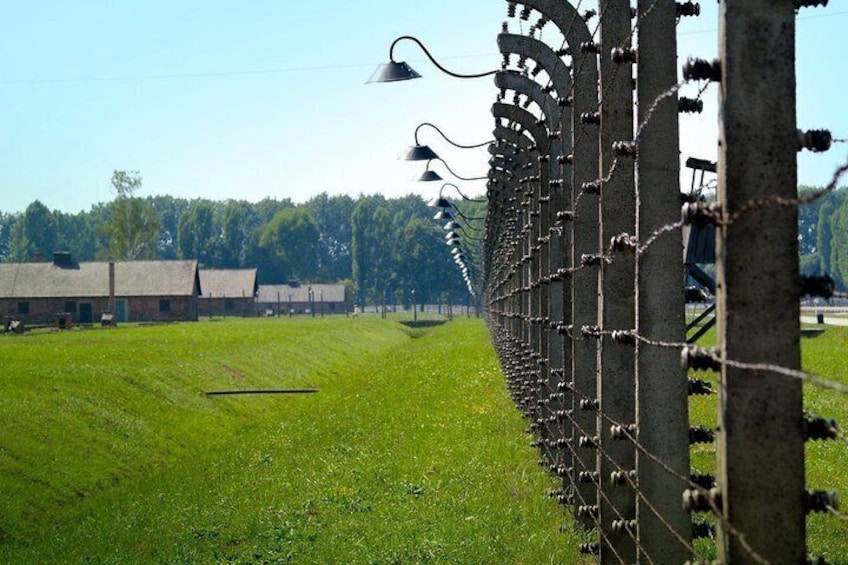 Een prikkeldraadhek, een grasveld en een rij gebouwen in de verte. 2