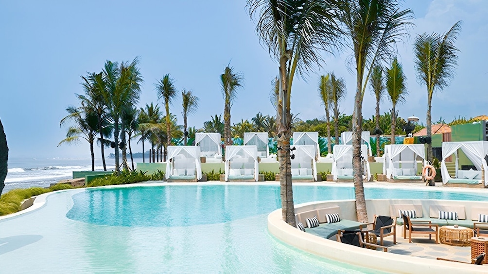 Ein Pool mit weißen Cabanas, Palmen und Blick auf den Ozean. 4