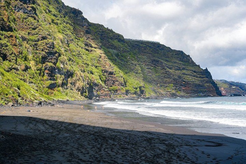 A beach with waves, a rocky cliff, and a cloudy sky. 2