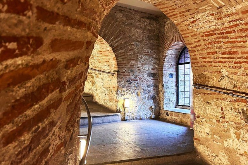 An arched stone corridor with a metal railing, a window, and a person standing in the distance. 5