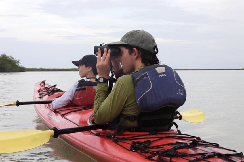 Two people in a red kayak on calm water, wearing life jackets and paddles. 5