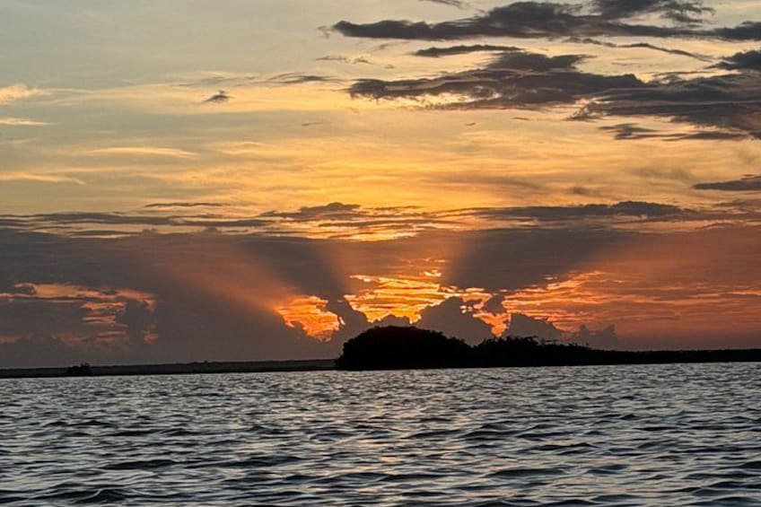 A sunset over a body of water with clouds and a silhouette of land in the distance. 3