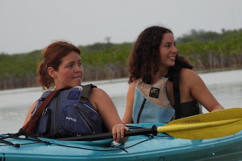 Two people kayaking on a calm body of water with greenery in the background. 4