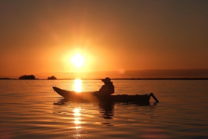 A sunset over a calm body of water with a person sitting on a boat. 2