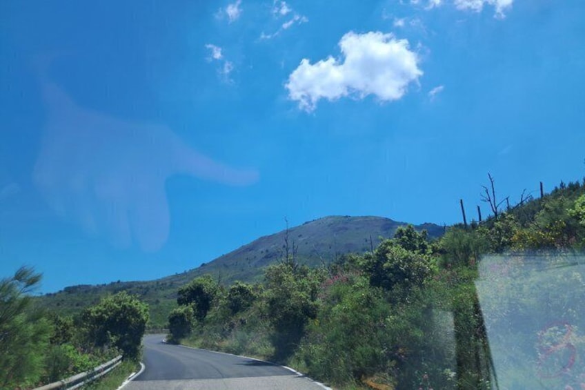 Eine kurvenreiche Straße durch eine hügelige Landschaft, im Hintergrund ein Berg. 4