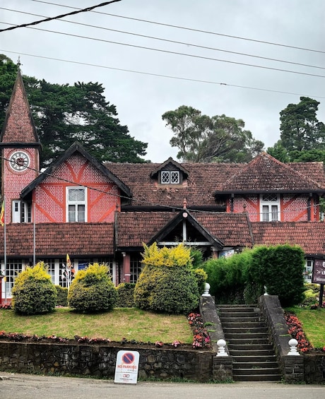 A red brick building with a clock tower, a steeply pitched roof, and a 'No Parking' sign in front. 4