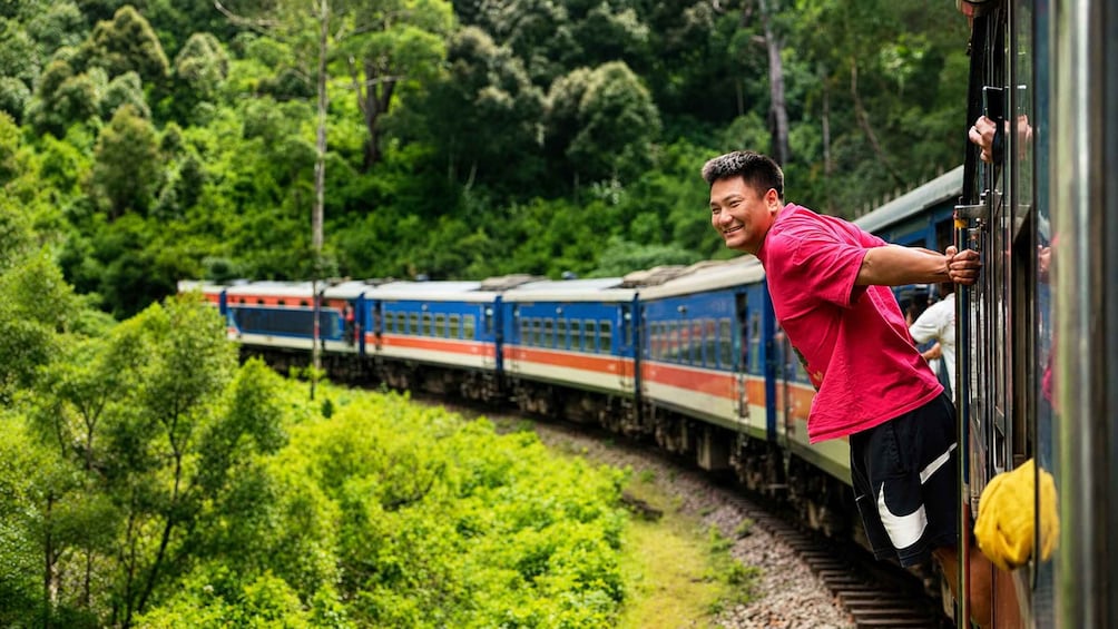 A person leaning out of a train window, with a forested landscape in the background. 3
