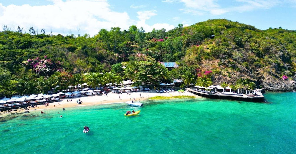 A tropical beach with clear turquoise waters, a dock, and lush greenery. 1