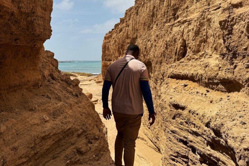 Eine Person geht durch eine schmale Schlucht, in der Ferne ist ein Strand zu sehen. 1