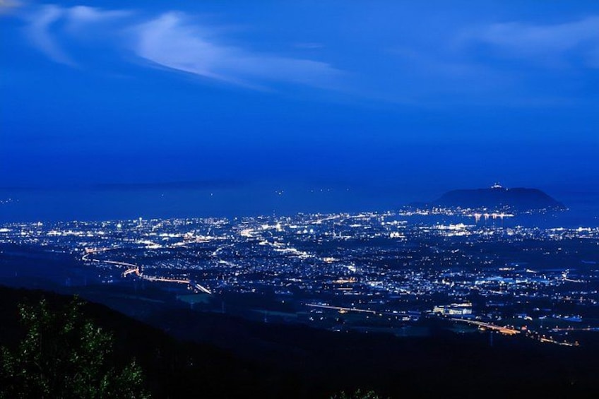 Un paisaje urbano nocturno con edificios iluminados y una montaña distante. 1