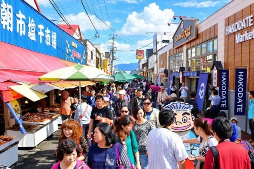 Una calle de mercado concurrida, gente comprando y vendedores ofreciendo productos. 4