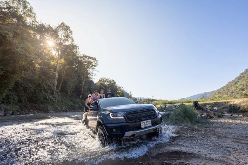 En lastbil kører gennem en lavvandet flod med mennesker på ladet. 2