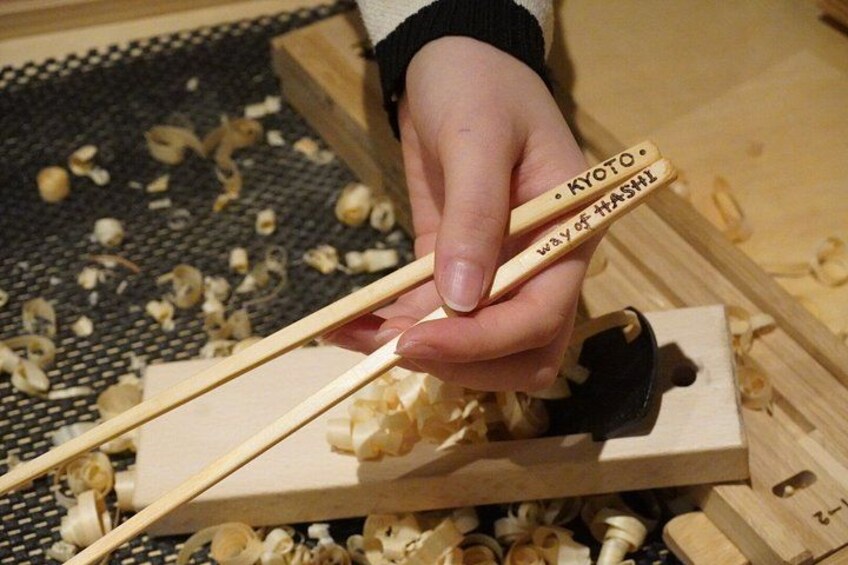 A person using chopsticks to handle wood shavings. 5