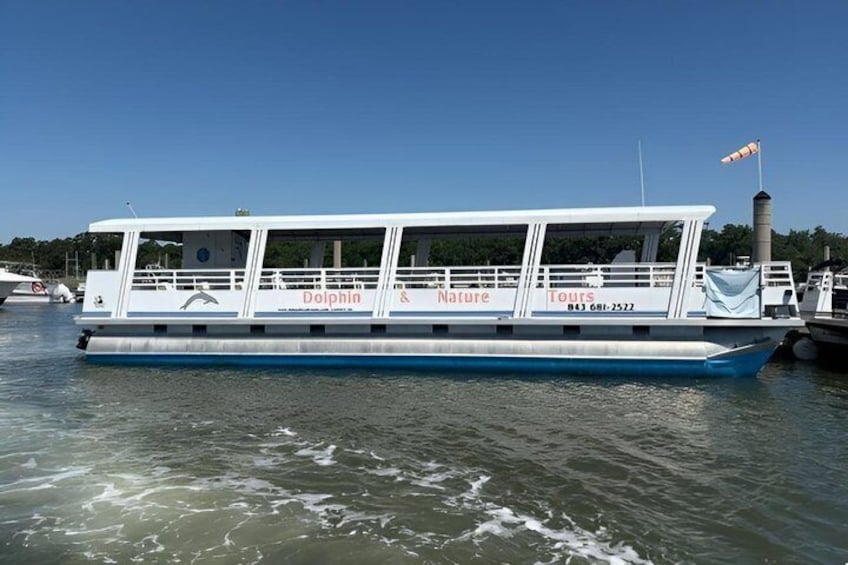 Una embarcación blanca y azul con la inscripción 'Dolphin & Nature Tours' en el costado, amarrada en un puerto deportivo. 3