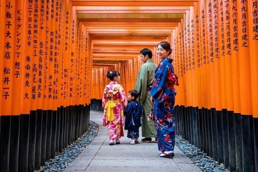 Een gezin loopt door een gang met oranje torii poorten, versierd met Japanse teksten. 1