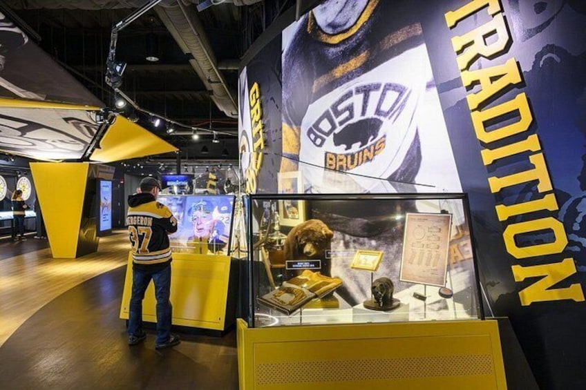 En udstilling med sportsmemorabilia, inklusive en Boston Bruins trøje og et glasmontre med diverse genstande. 2