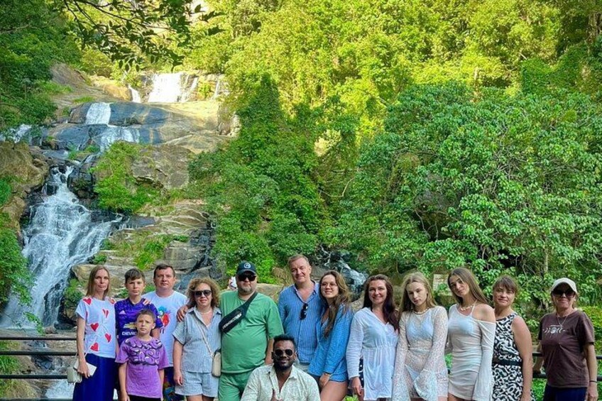 A group of people standing in front of a waterfall surrounded by lush greenery. 4