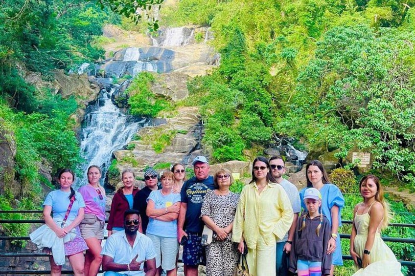 A group of people standing in front of a waterfall surrounded by greenery. 2