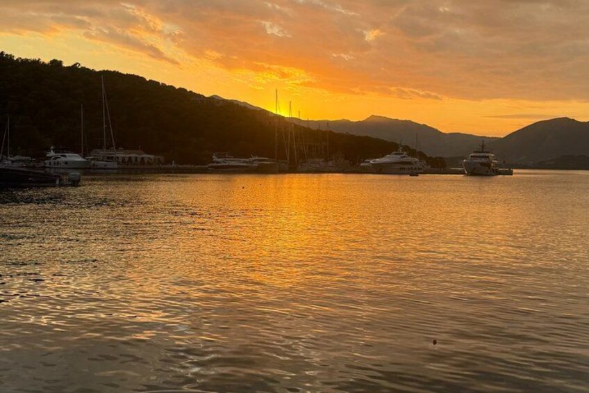 Ein Sonnenuntergang über ruhigem Wasser, mit Booten und einer Bergkulisse im Hintergrund. 3