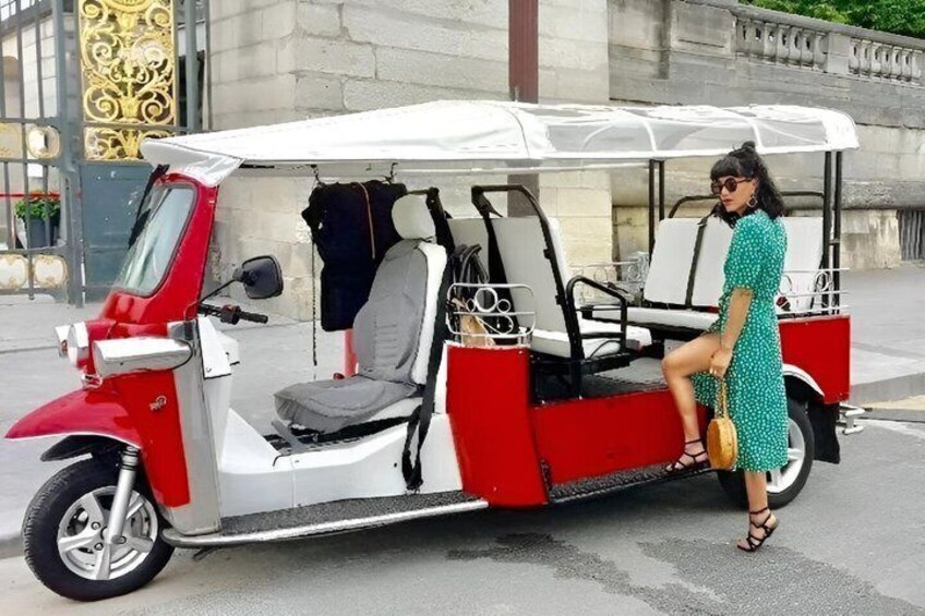 Un véhicule à trois roues, de couleur rouge et blanche, doté d’une cabine fermée, d’un siège passager et d’un espace de chargement. 3