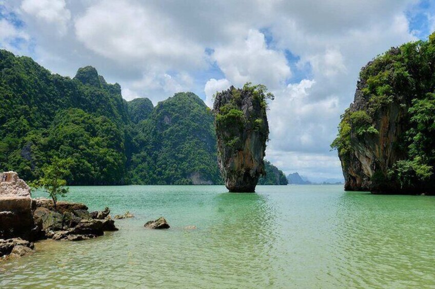 A calm sea with two prominent limestone pillars surrounded by lush greenery. 4