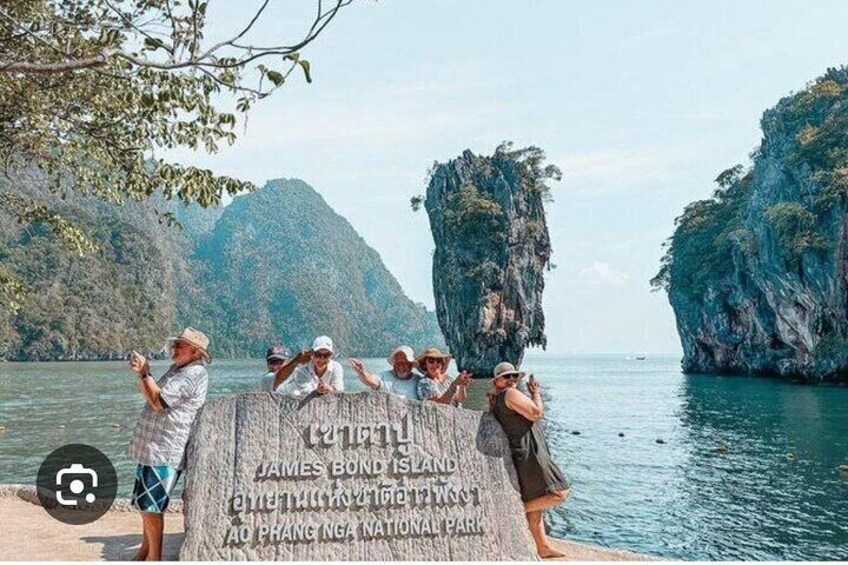 A group of people standing by a sign at James Bond Island, overlooking the water and limestone cliffs. 5