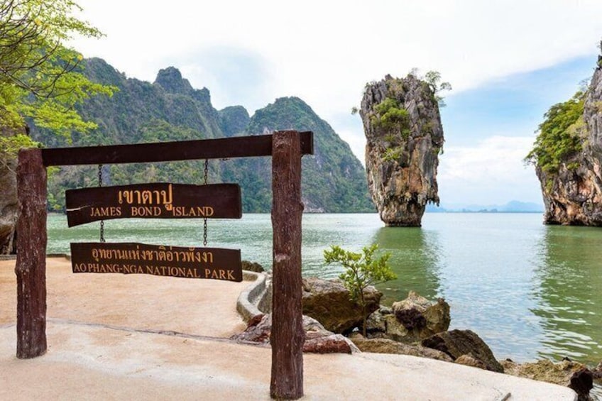 A wooden signpost with Thai text, a rocky island, and calm water. 1