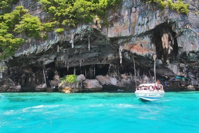 A boat with passengers on turquoise water near a rocky cliff with vegetation. 2