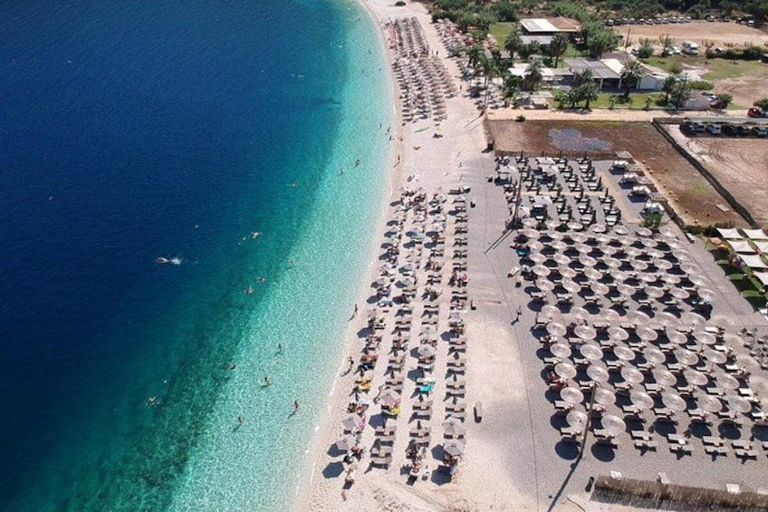 Ein Strand mit Reihen von Sonnenschirmen und Liegestühlen, ein sandiger Uferstreifen und ein klares, blaues Meer. 5