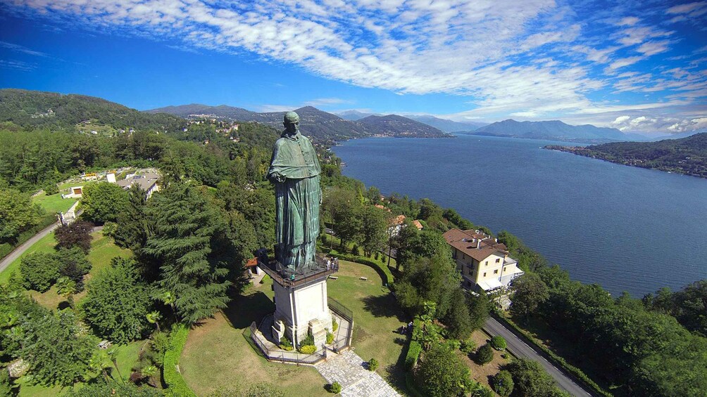 A statue on a pedestal surrounded by greenery, overlooking a lake with mountains in the background. 1