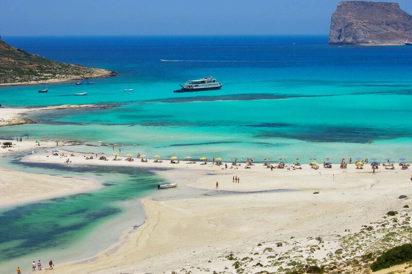 A beach with clear turquoise waters, a boat, and a rocky outcrop in the distance. 1