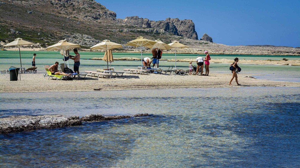 A beach with people sunbathing, umbrellas, and clear water. 2
