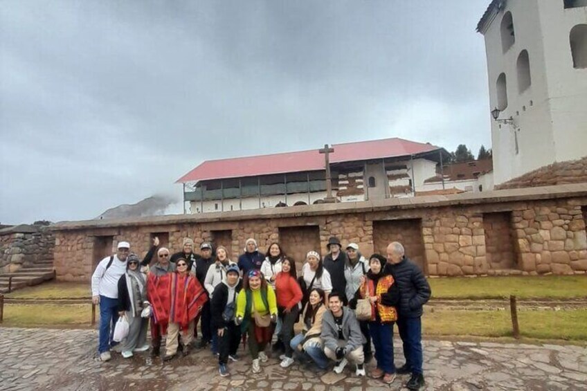 A group of people posing in front of a building with a red roof and stone walls. 4