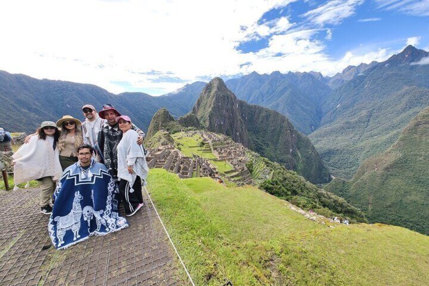 A group of people standing on a paved area with a view of Machu Picchu ruins and surrounding mountains. 1