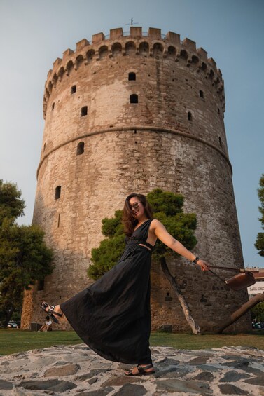 A woman in a black dress standing in front of a historic stone tower. 5