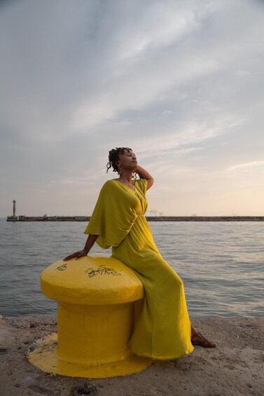 A person in a yellow dress sitting on a yellow object by the water with a lighthouse in the background. 4