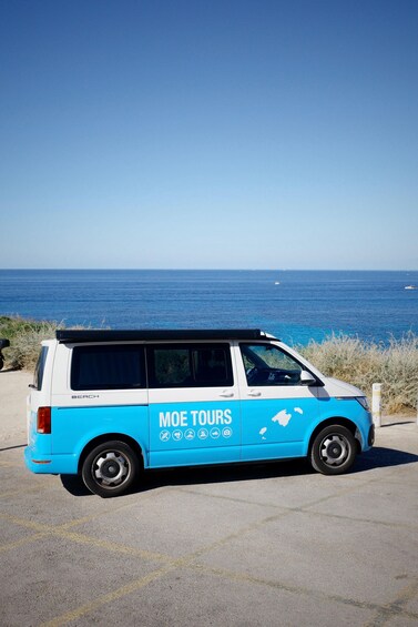 A blue van parked on a coastal road with the ocean and a clear sky in the background. 3